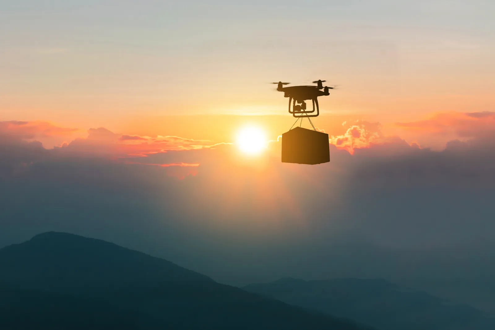 Drone carrying a package over mountains at sunrise