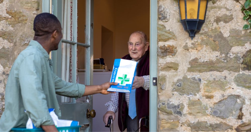 Local pharmacy courier gives medication in a pharmacy-branded package to an older man